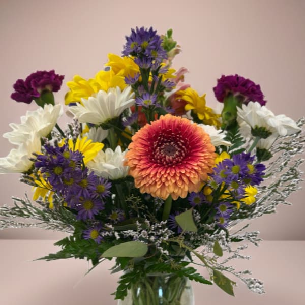 Mixed bouquet in a glass vase with purple, yellow, white, and peach flowers.