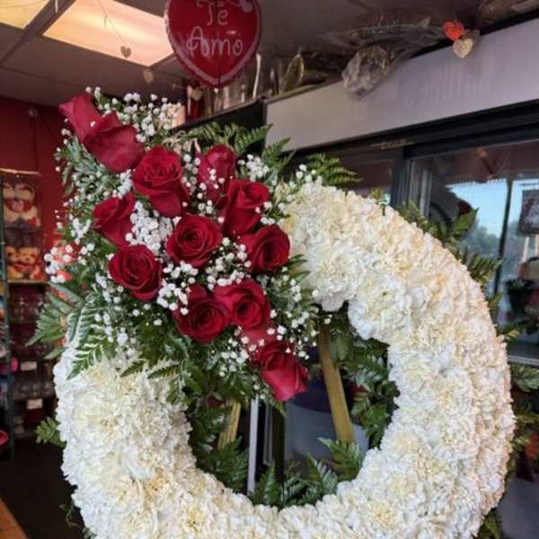 Heart-shaped floral wreath with red roses and white flowers on an easel