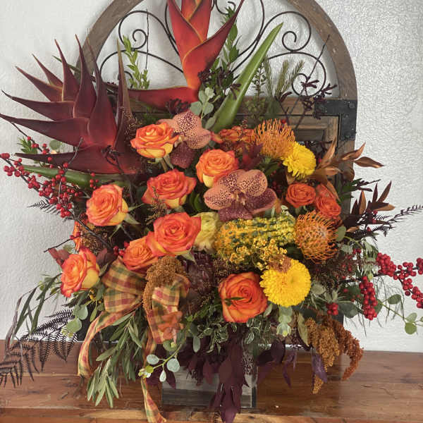 Mixed floral arrangement with orange roses and tropical blooms in a decorative container