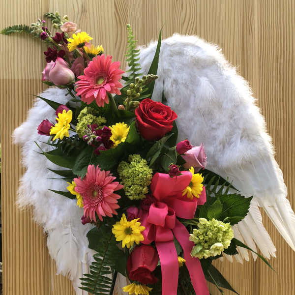 Floral standing spray with pink and red roses, gerbera daisies, and white wings