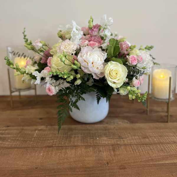 Pink and white floral arrangement in a white vase with candles beside it