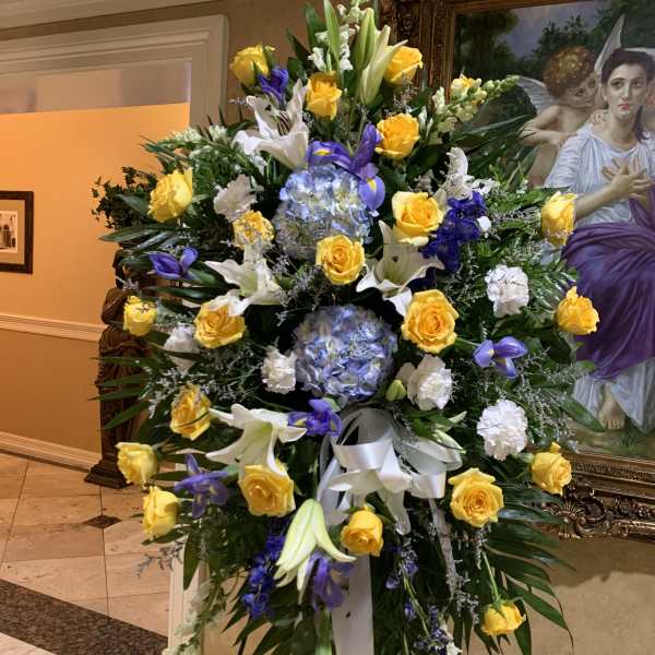 Large standing floral spray with yellow roses, white lilies, and purple blooms