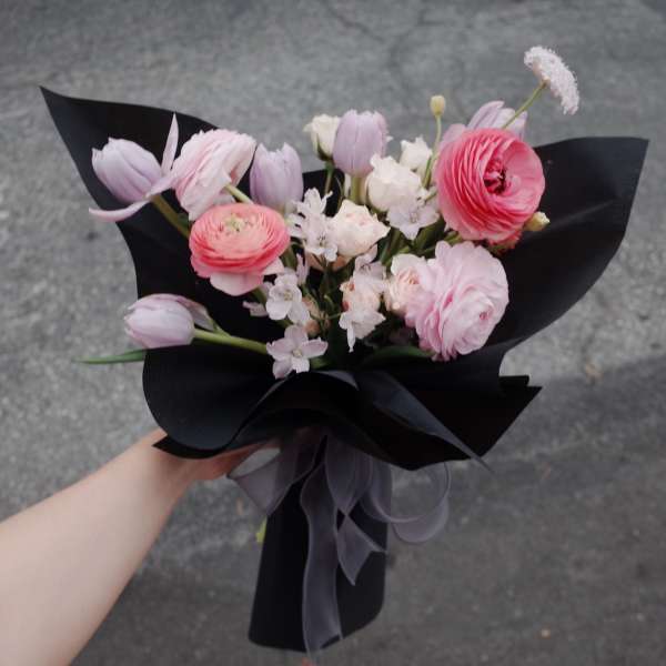 Hand-tied bouquet of pink and white flowers wrapped in black paper