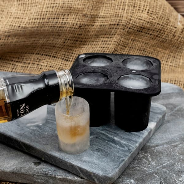 Bottle pouring liquor into a frosted shot glass beside an ice mold