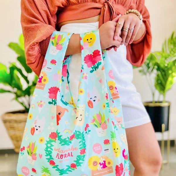 Reusable pastel tote bag with cute floral and character illustrations held by a person indoors