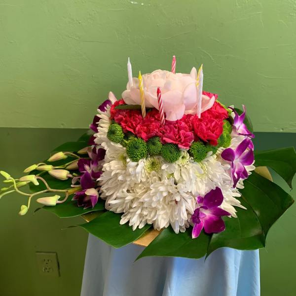 Round floral cake with candles, white chrysanthemums, pink blooms, and purple orchids