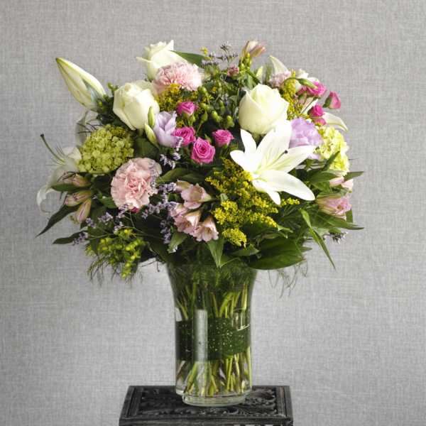 Mixed bouquet of white lilies, roses, and pink flowers in a glass vase