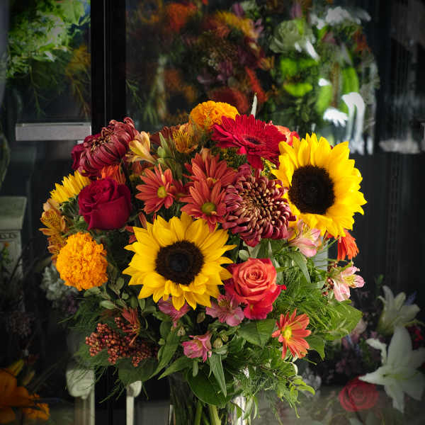 Mixed bouquet of sunflowers, roses, and chrysanthemums in a glass vase