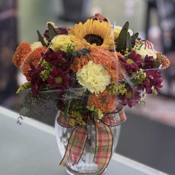 Mixed bouquet with a sunflower in a glass vase and plaid ribbon