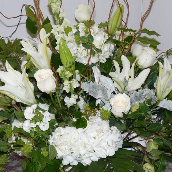 Large white floral arrangement with lilies, roses, and hydrangeas