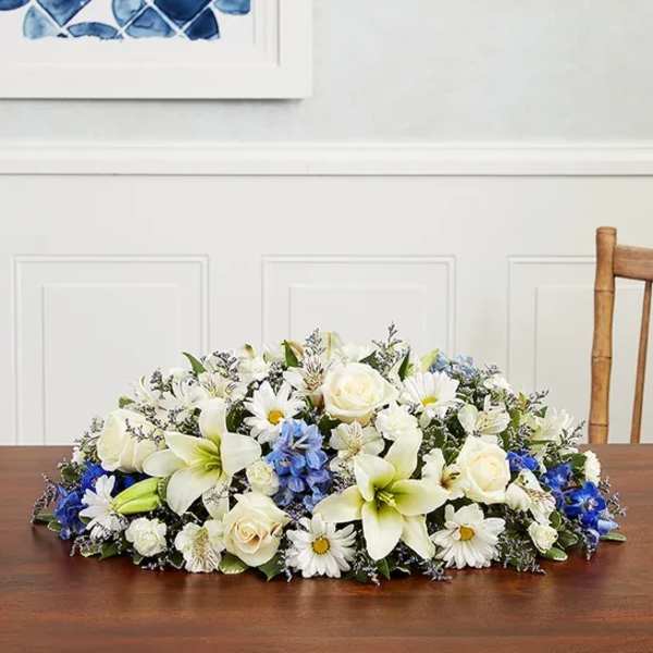 Low floral centerpiece with white lilies, roses, and daisies on a table