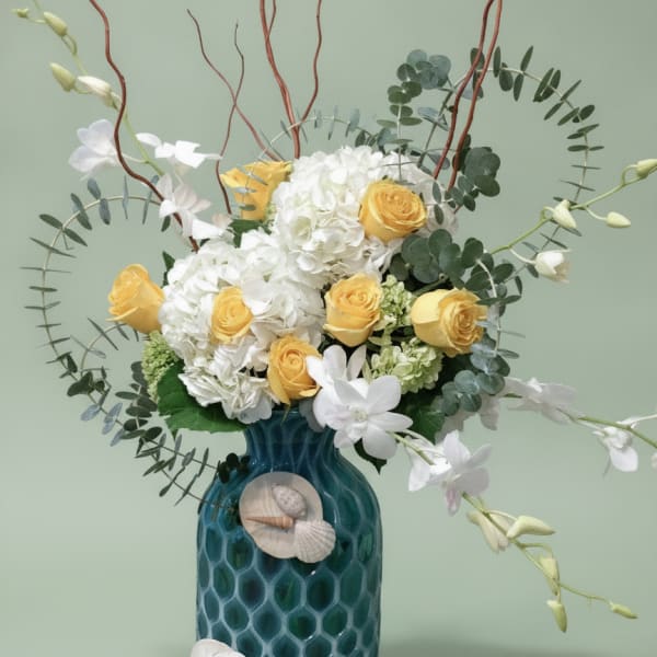 Yellow roses and white hydrangeas in a blue vase with shell accents