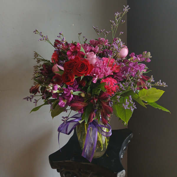 Mixed bouquet of red and pink flowers in a glass vase with a purple ribbon