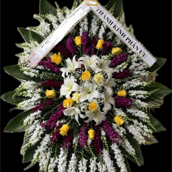 Large standing floral wreath with white lilies, yellow roses, and purple flowers