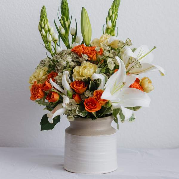 Orange roses and white lilies arranged in a ceramic vase