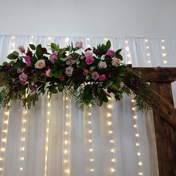 Floral garland with pink and burgundy roses on a wooden arch