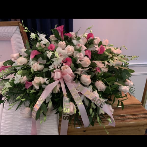 Large pink and white floral spray with ribbon on a casket
