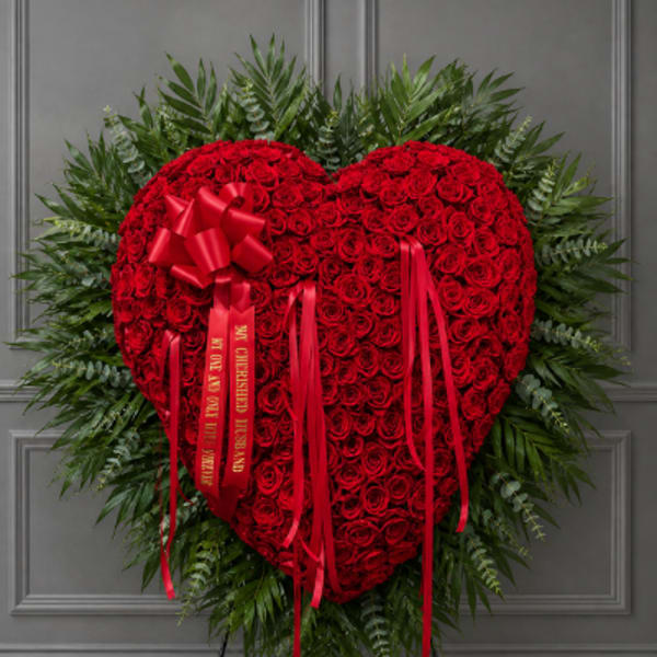 Heart-shaped red rose wreath with red ribbons on a stand
