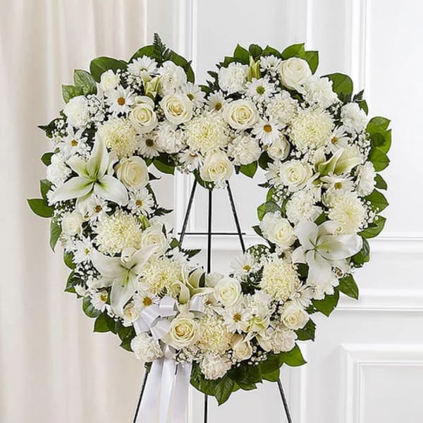 Heart-shaped white floral wreath on an easel with a ribbon bow