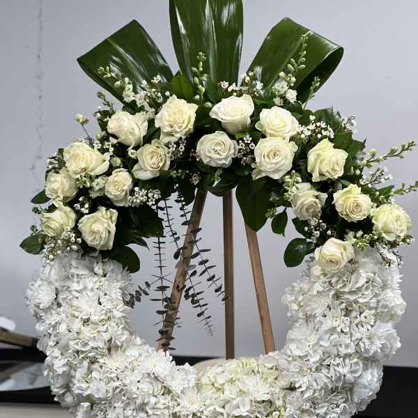 White rose and hydrangea wreath on an easel with dark green leaves