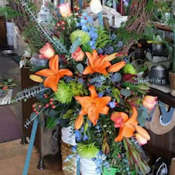 Tall floral wreath with orange lilies and mixed blooms on a stand