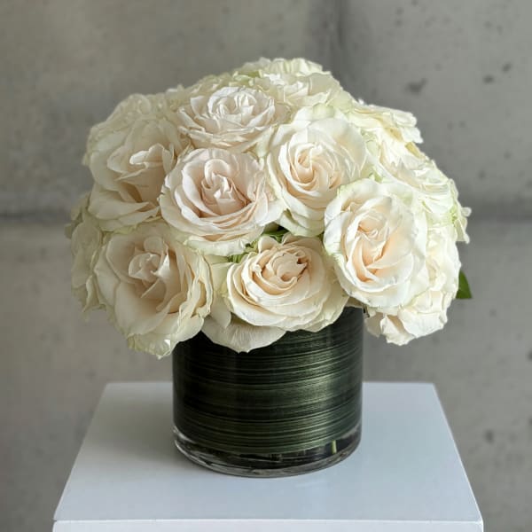 White roses arranged in a dark glass vase on a white pedestal