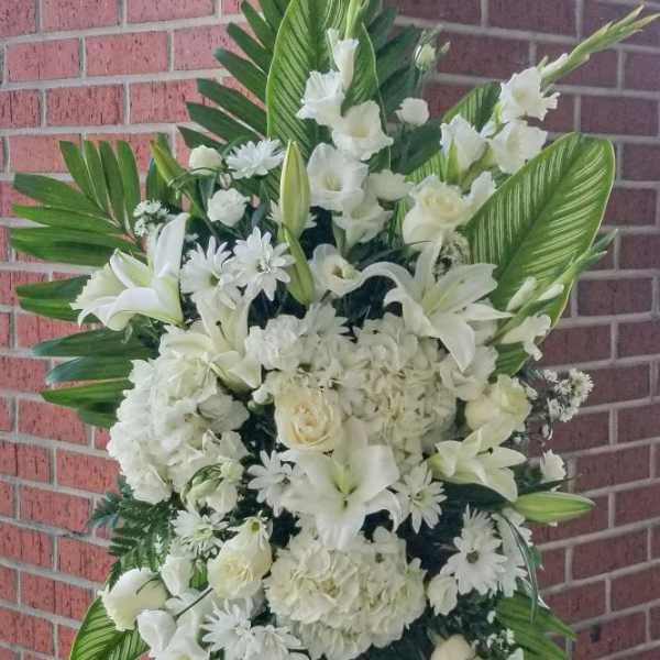 White funeral spray with lilies, roses, and daisies on an easel