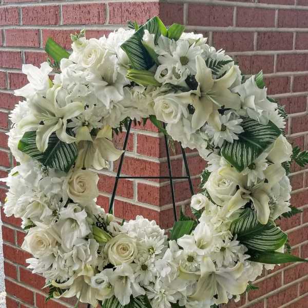 White floral wreath on a black stand against a brick wall