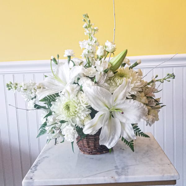 White floral arrangement in a wicker basket with lilies and chrysanthemums
