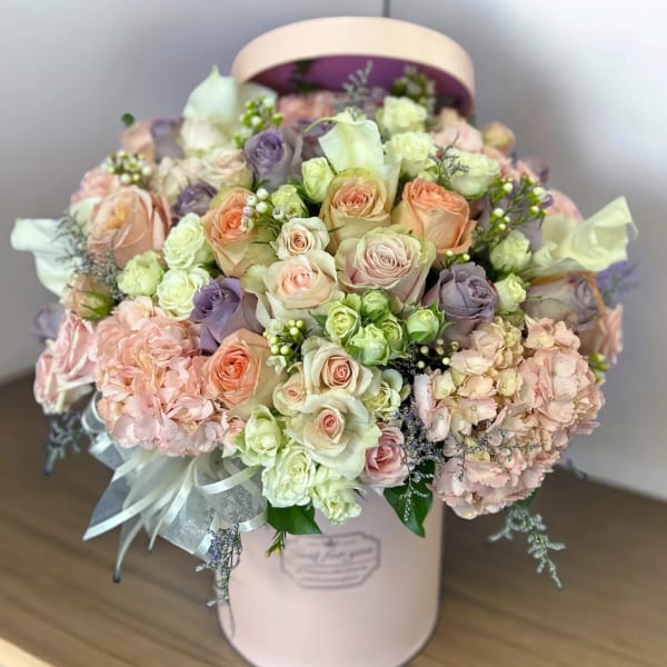Pastel roses and hydrangeas arranged in a pink hat box with ribbon