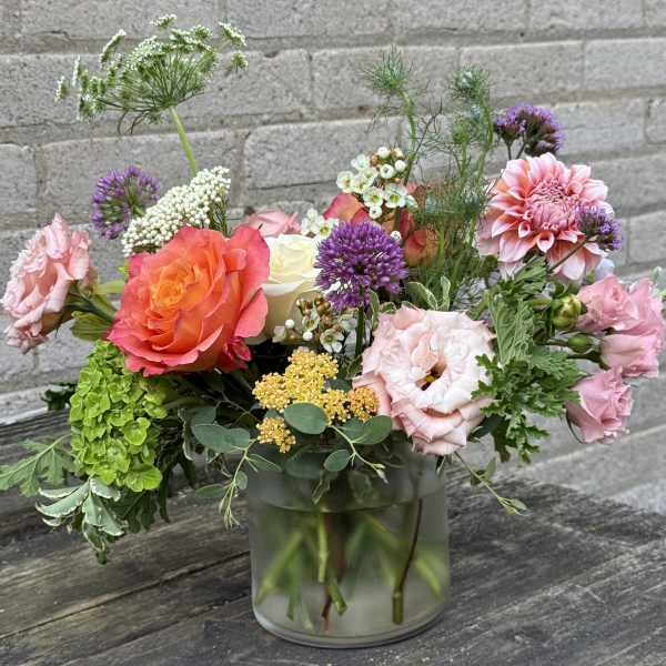 Mixed bouquet of pink, orange, purple, and white flowers in a glass vase