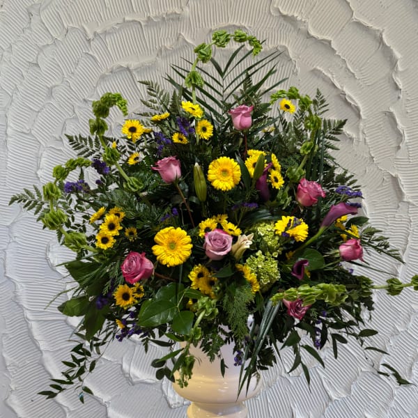 Mixed bouquet with pink roses, yellow daisies, and purple accents in a white vase