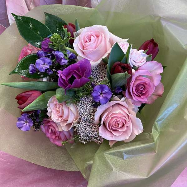 Bouquet of pink and purple roses with small purple flowers wrapped in paper