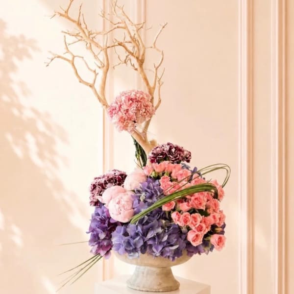 Pink and purple floral arrangement in a pedestal vase with bare branches