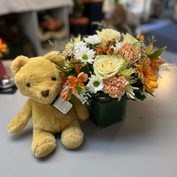 Teddy bear beside a mixed flower arrangement in a green vase