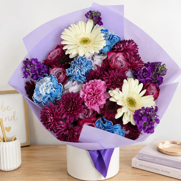 Mixed bouquet of purple, pink, blue, and white flowers in a white box
