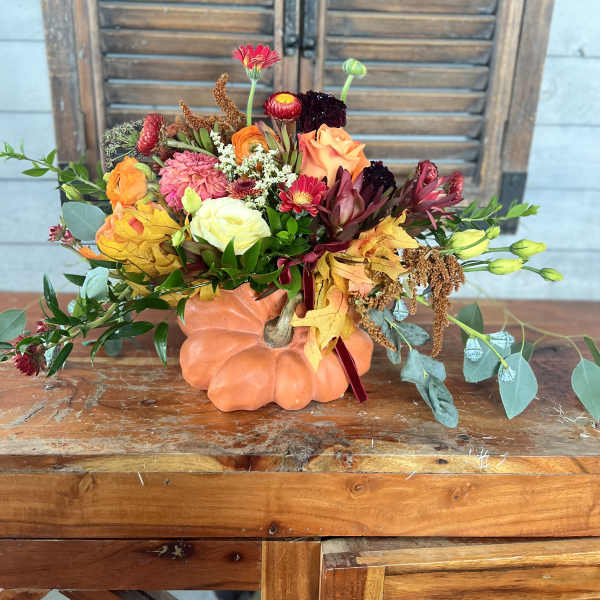 Autumn floral arrangement in a pumpkin-shaped container with orange, pink, and burgundy blooms
