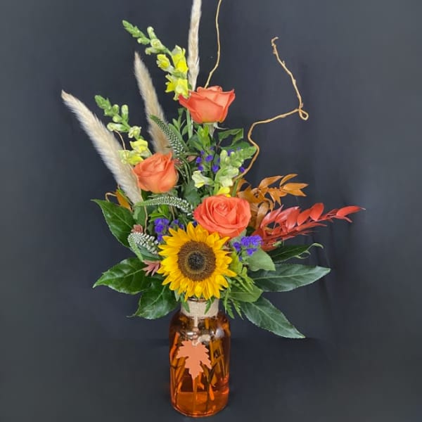 Sunflower and orange rose arrangement in an amber glass jar