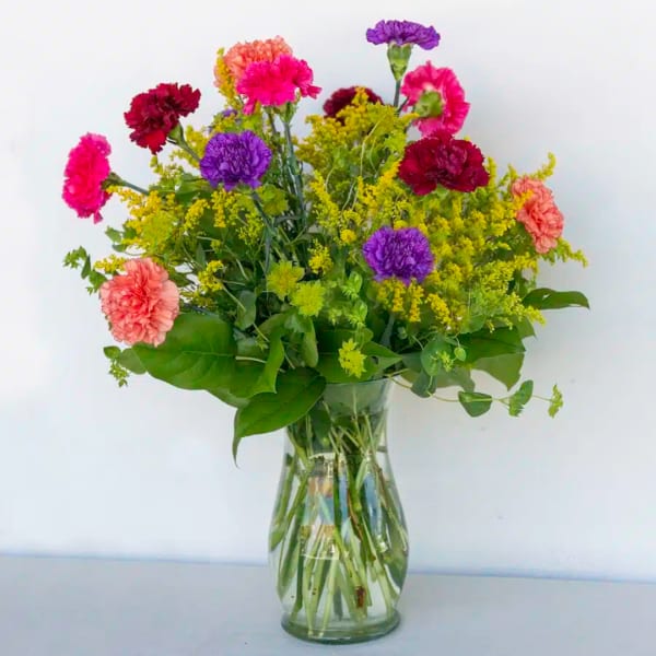 Mixed bouquet of carnations and filler flowers in a clear glass vase