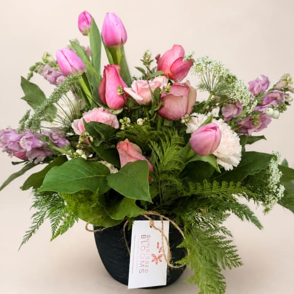 Pink tulips and roses arranged in a black pot with greenery