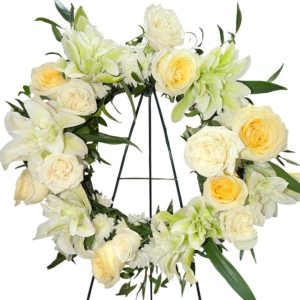 White floral wreath with pale yellow roses on a black stand