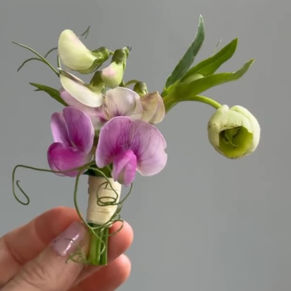 Small purple and white boutonniere with a hand holding it