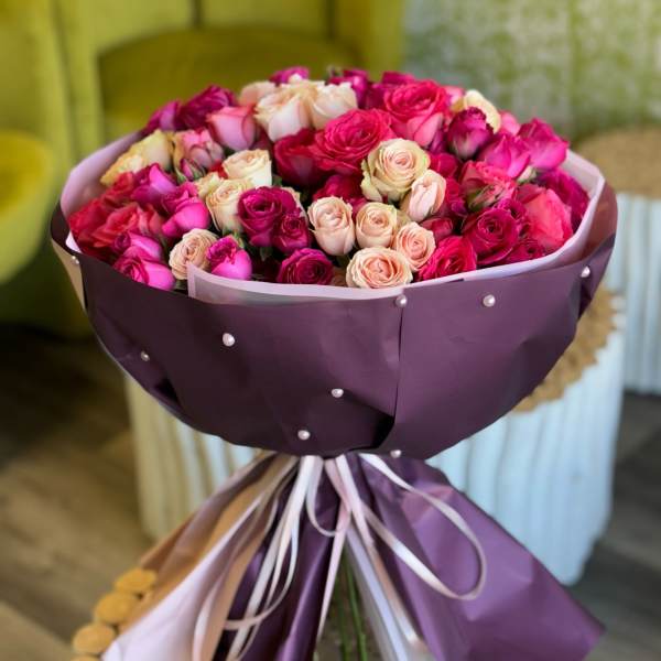 Bouquet of pink and cream roses wrapped in purple paper