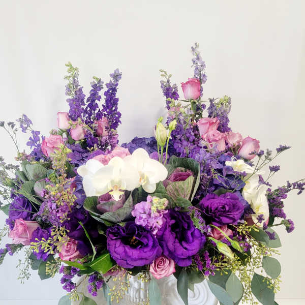 Purple and pink floral arrangement with white orchids in a white vase