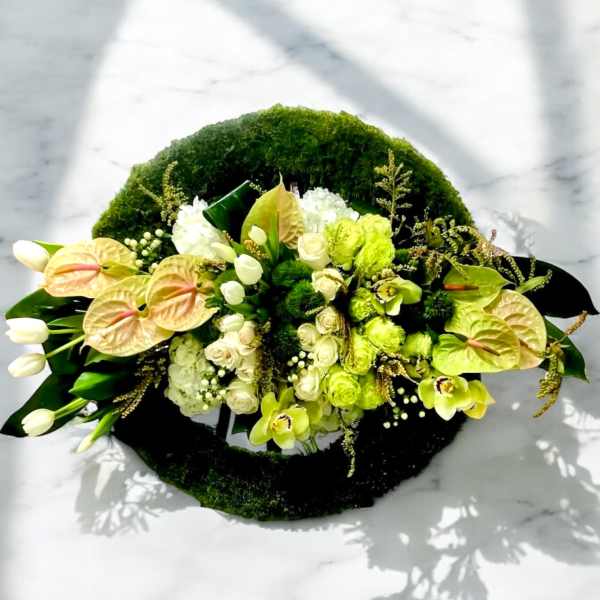 Green and white floral arrangement with anthuriums and roses on a moss base