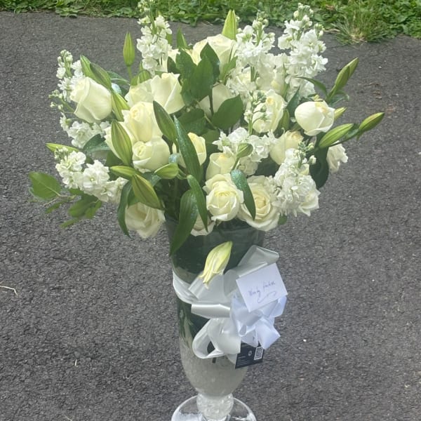 White roses and lilies arranged in a tall glass vase with a white ribbon.