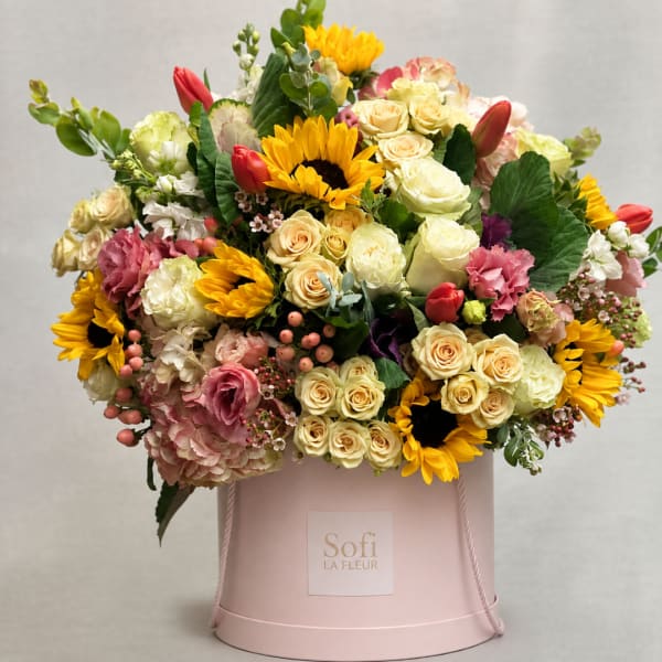 Mixed bouquet of sunflowers, roses, and tulips in a pink hatbox