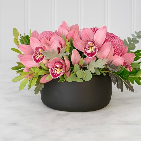 Pink orchid arrangement in a black bowl vase