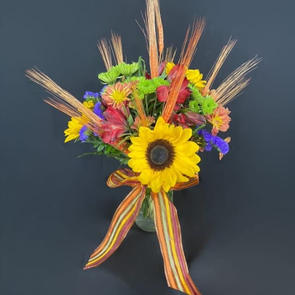 Bright mixed bouquet with a sunflower in a glass vase and striped ribbon