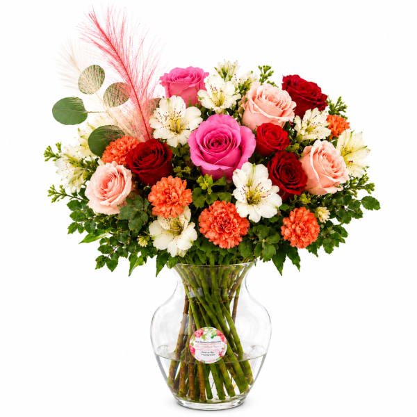Mixed bouquet of roses, alstroemeria, and carnations in a clear glass vase
